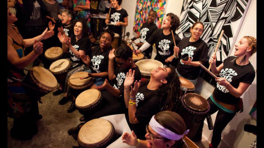 Bele Bele Rhythm Collective members drumming while wearing matching black T-shirts