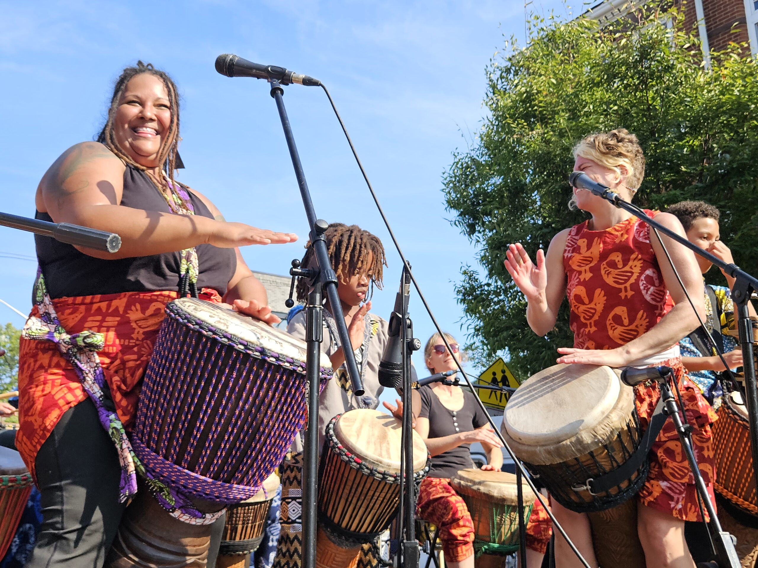 Ayanna and Kristen drumming on stage outdoors in Baltimore on a beautiful, sunny day.