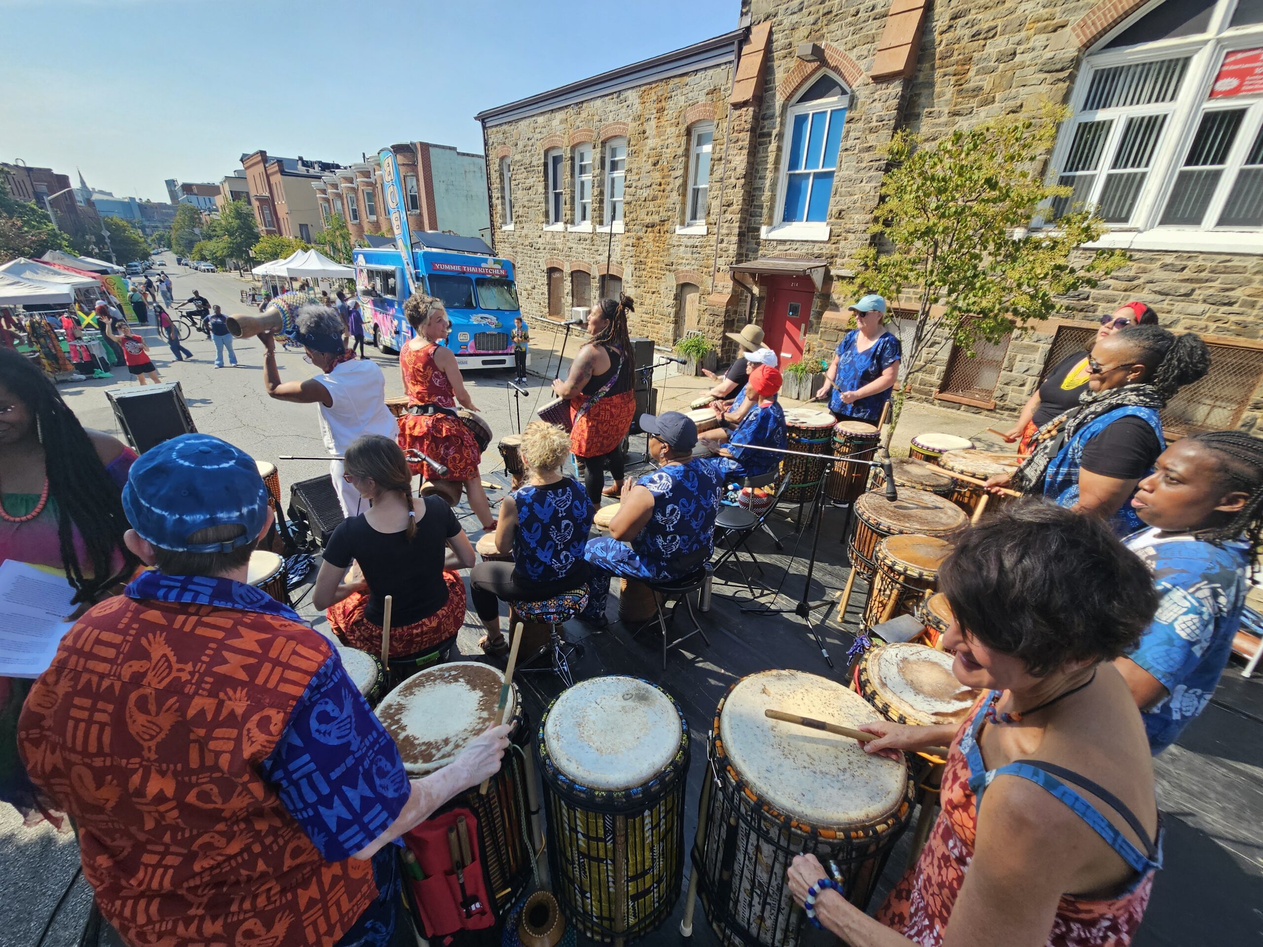 A view of Bele Bele performing at an outdoor festival from the stage perspective, looking out toward the audience at a street festival.