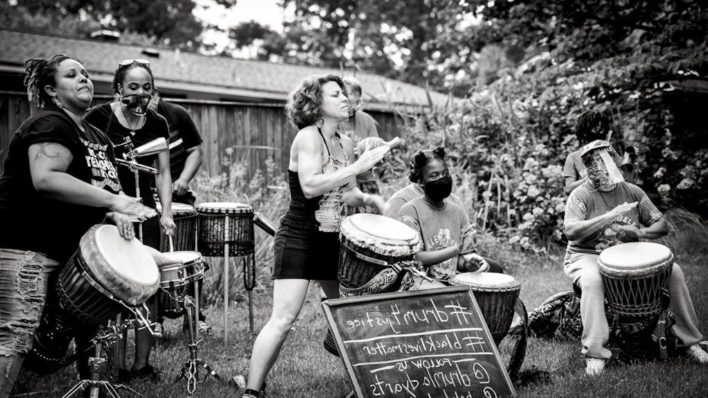 Black and white photo of Bele Bele Rhythm Collective members drumming outdoors