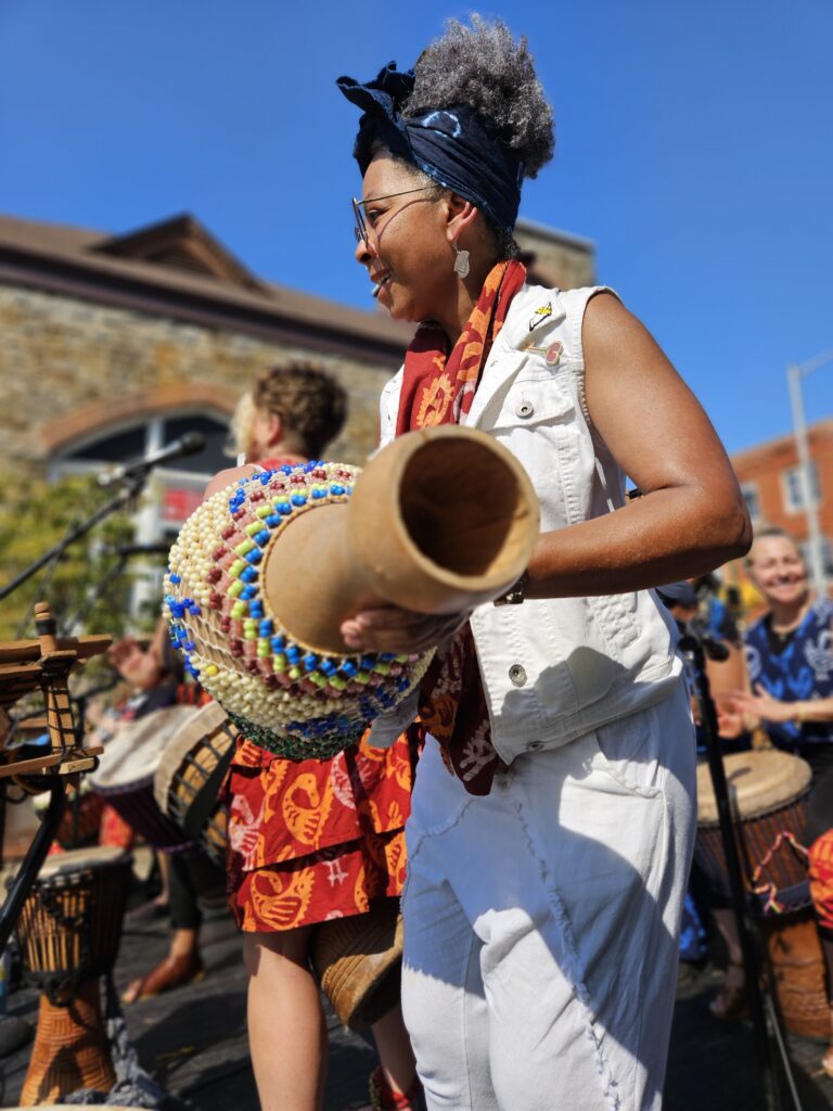 A woman from Bele Bele holds a drum and performs at an outdoor performance in Baltimore