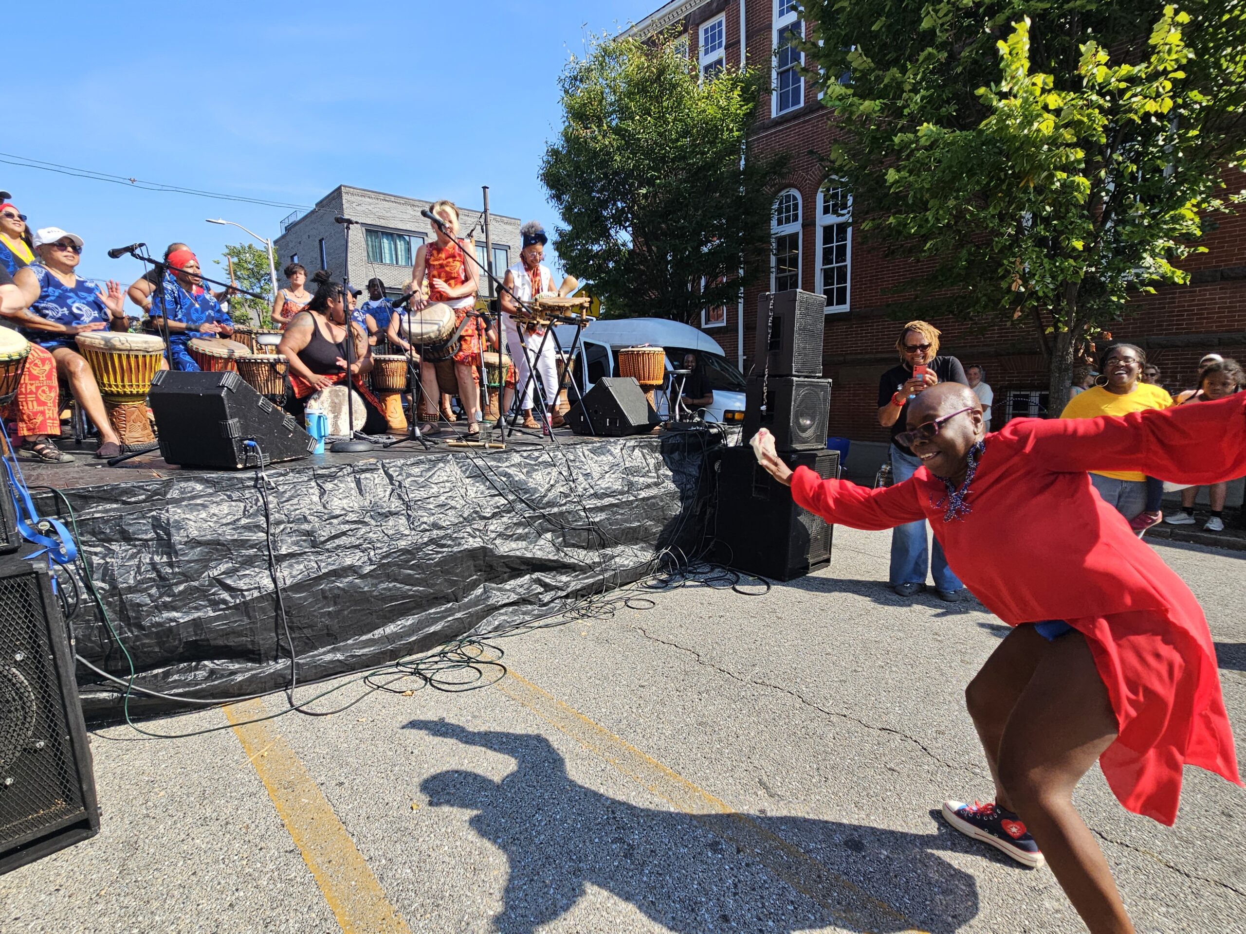 A woman wearing red dances energetically while Bele Bele performs on an outdoor stage in Baltimore