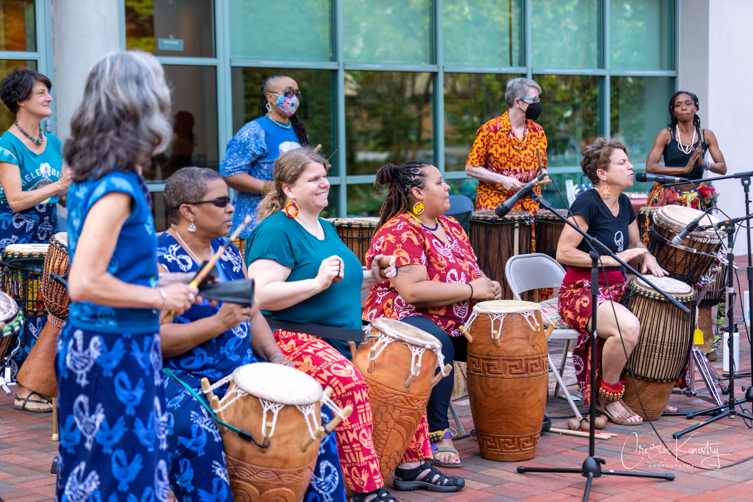 Bele Bele Rhythm Collective performing on drums in front of a glass storefront window